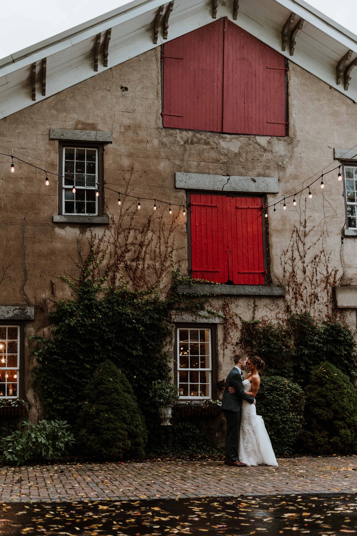 Newlywed couple kissing in front of a stone barn.