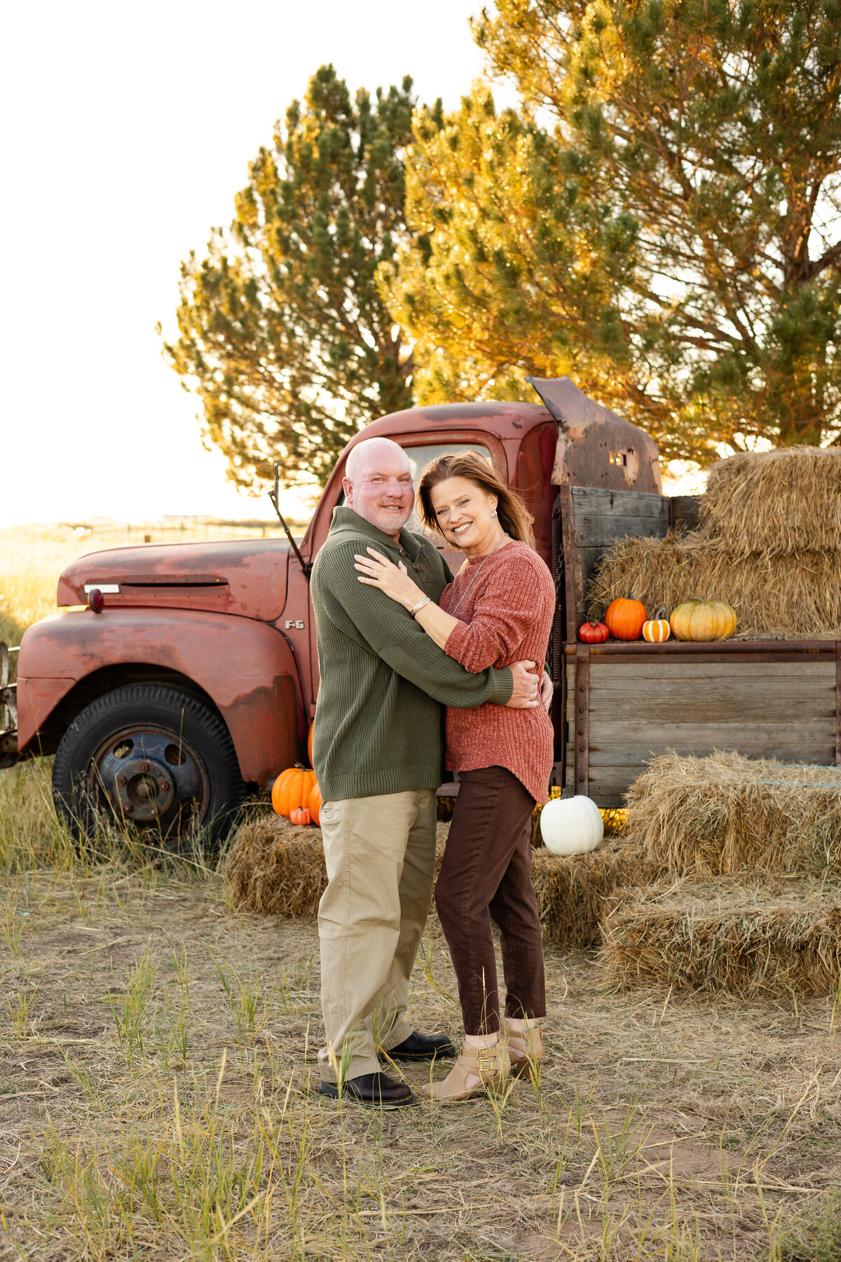 Husband and wife stand in front of a vintage red farm truck and smile at the camera.