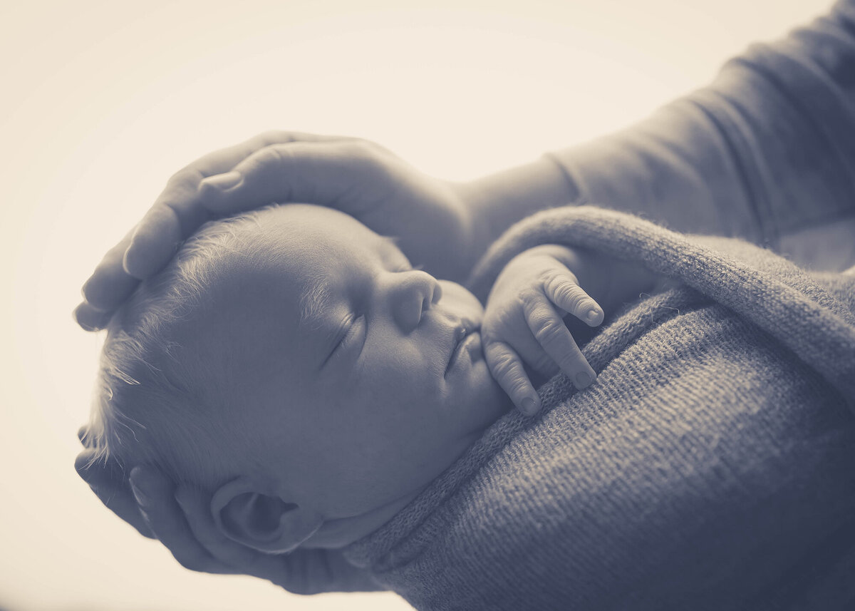 A newborn sleeps in a swaddle while cradled in a parent's hands