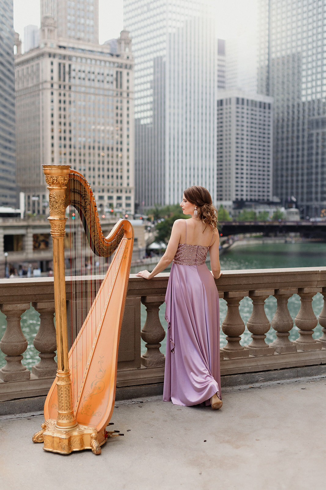 woman standing at overlook at Chicago River. She is wearing a lavender gown and standing next to a gold harp.