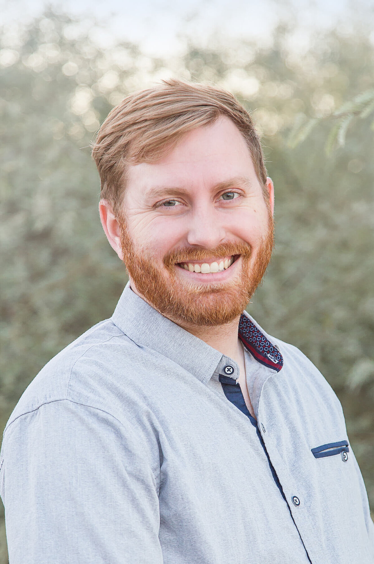 Redheaded man with short beard in a light blue shirt smiling