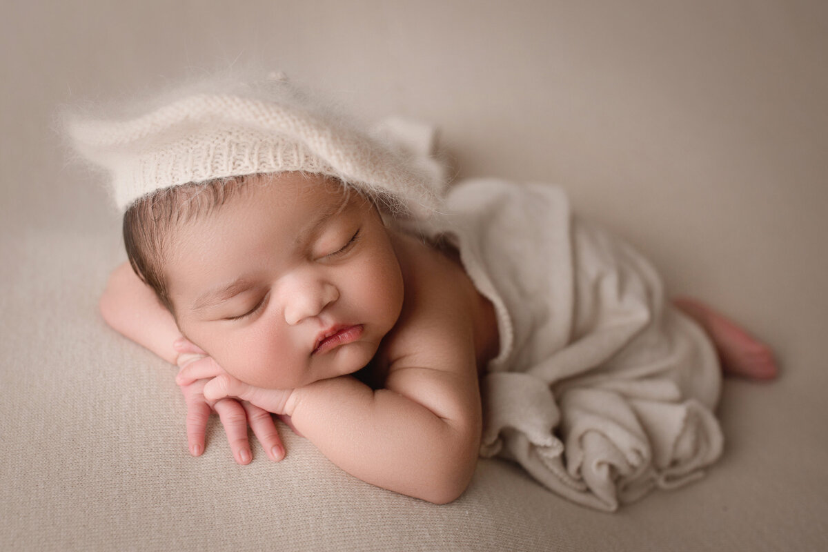 newborn girl sleeping wearing a cream hat and wrap