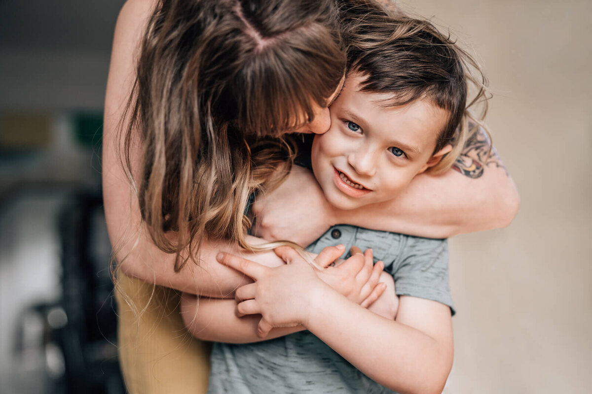 A small boy wraps his arms around his mother's, as she hugs him from behind during in in home photo session in Minneapolis.