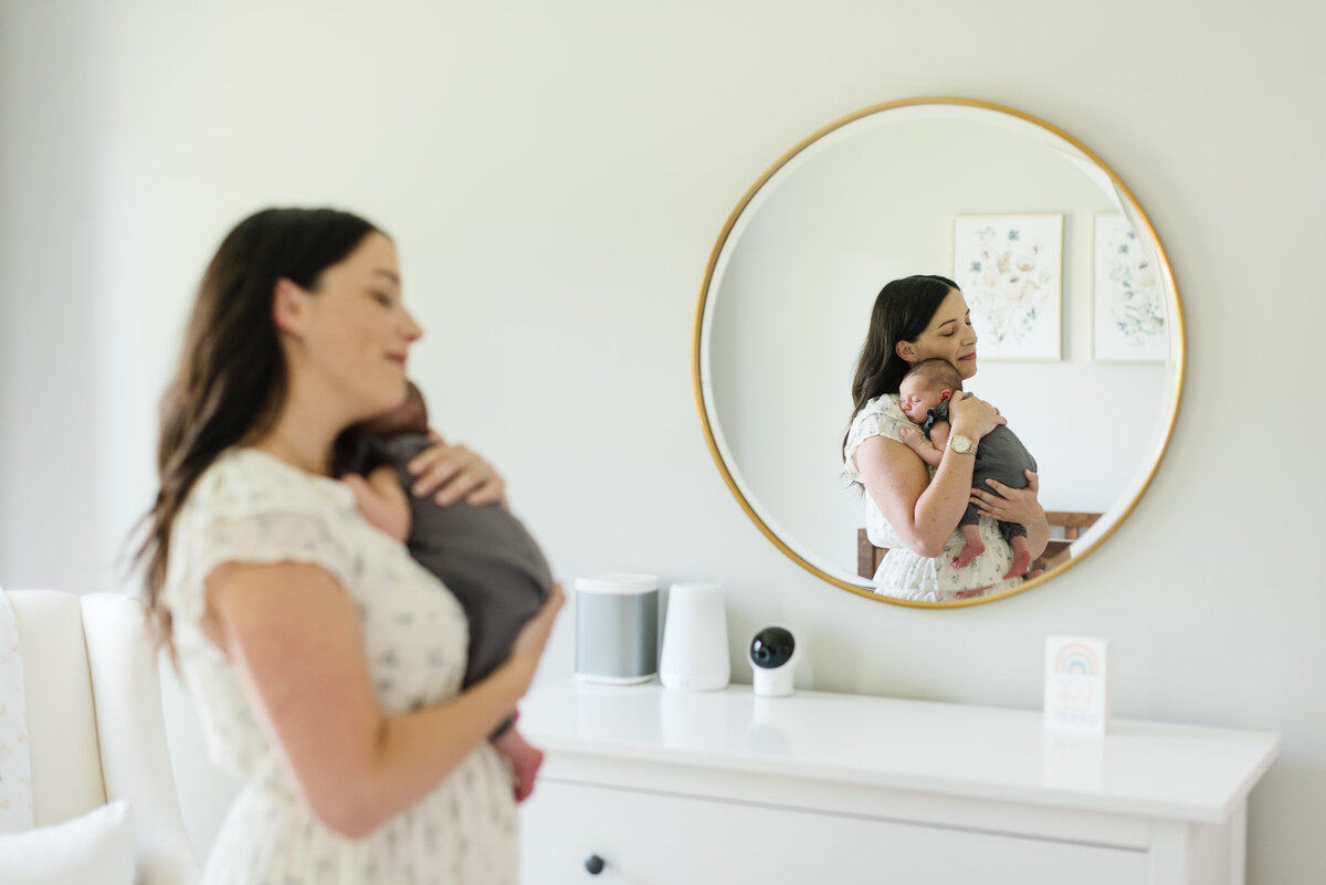 Mother holding her baby next to bathroom mirror