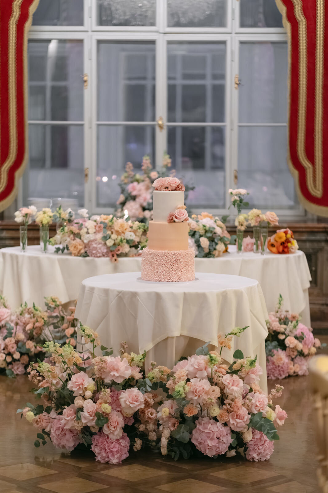 Luxury wedding cake displayed in the middle of the room surrounded by fresh flower arrangements