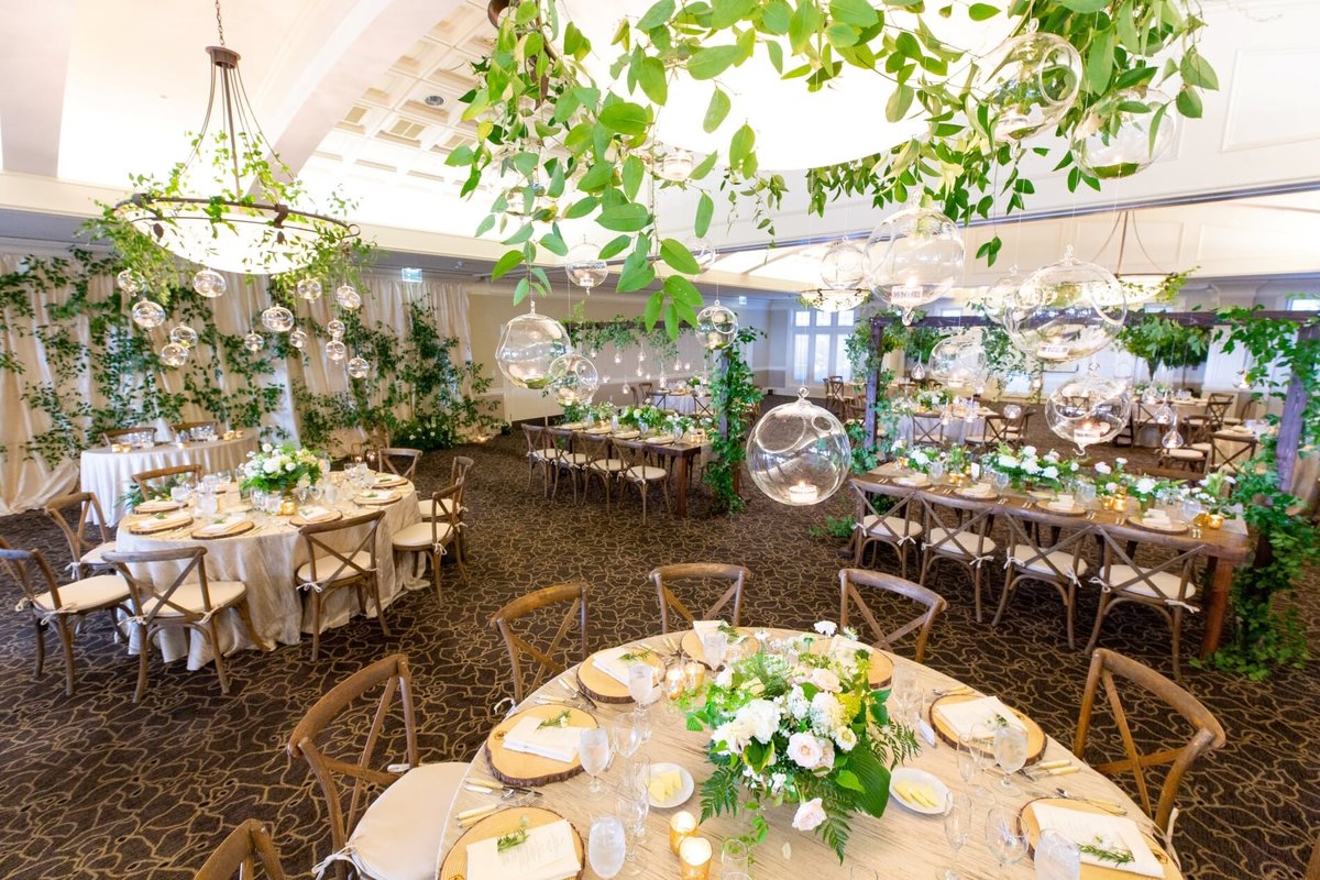 Newcastle wedding reception with round and rectangular wooden tables, Vineyard chairs, ivory linens, and greenery decor