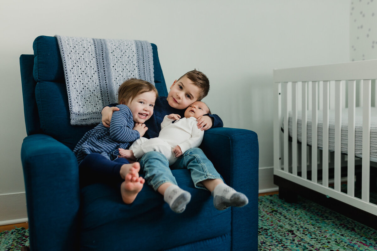 Family photoshoot with big siblings snuggle newborn on chair