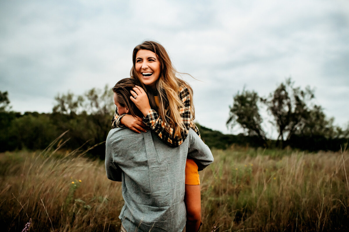 Couples Photography, a woman jumps into a mans arms laughing in a grassy field