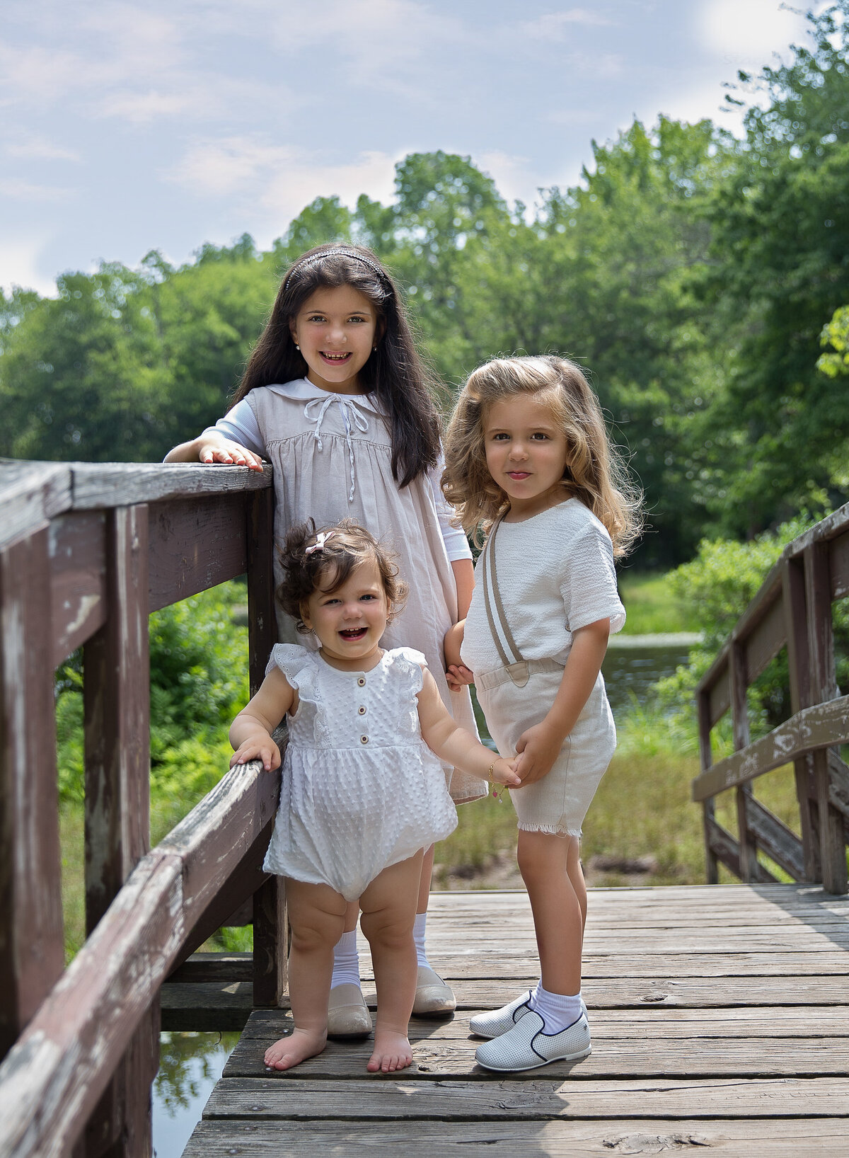 Three young siblings stand on a bridge in a brooklyn, ny park for a family photoshoot. Captured by Chaya Bornstein, Brooklyn Family Photographer