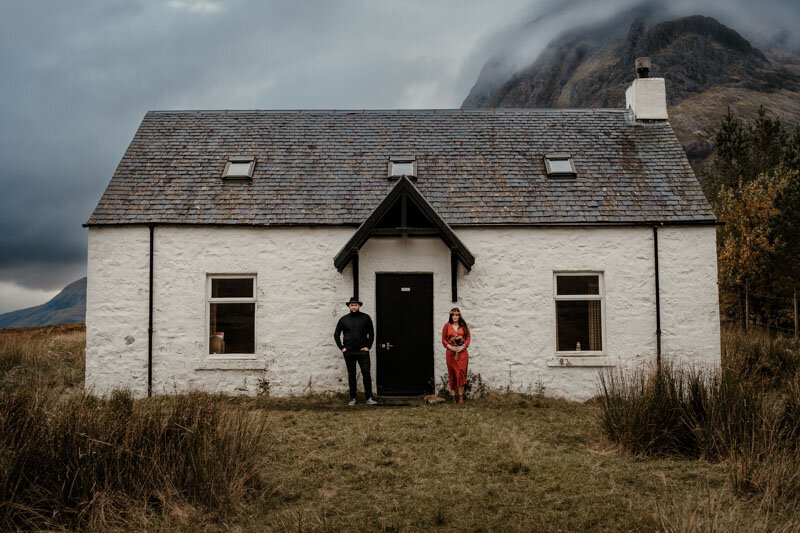 Séance photo de couple en Écosse devant la White House à Glencoe, dans une atmosphère brute et cinématographique au cœur des Highlands.