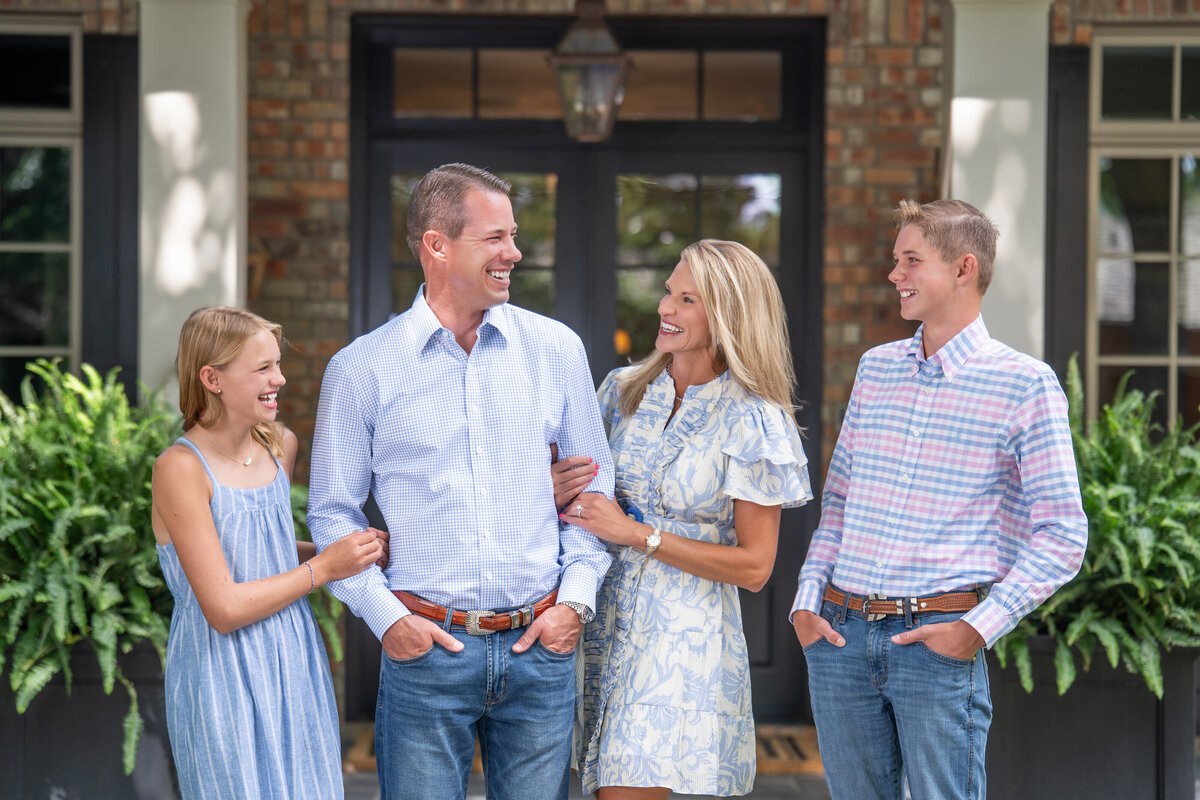 4 family members laugh candidly in front of their home for their family picture