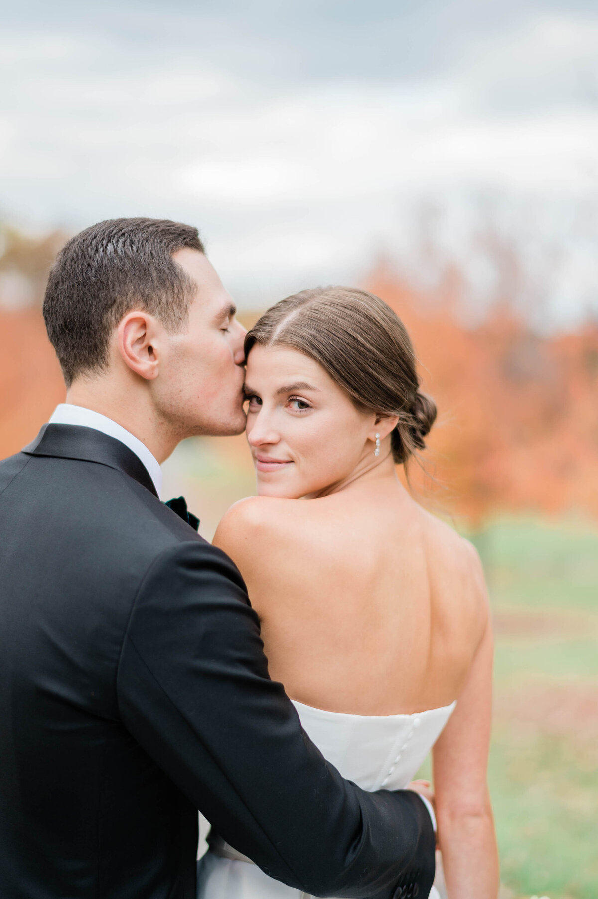 A romantic close-up of the groom kissing the bride’s forehead as she looks at the camera with a soft smile