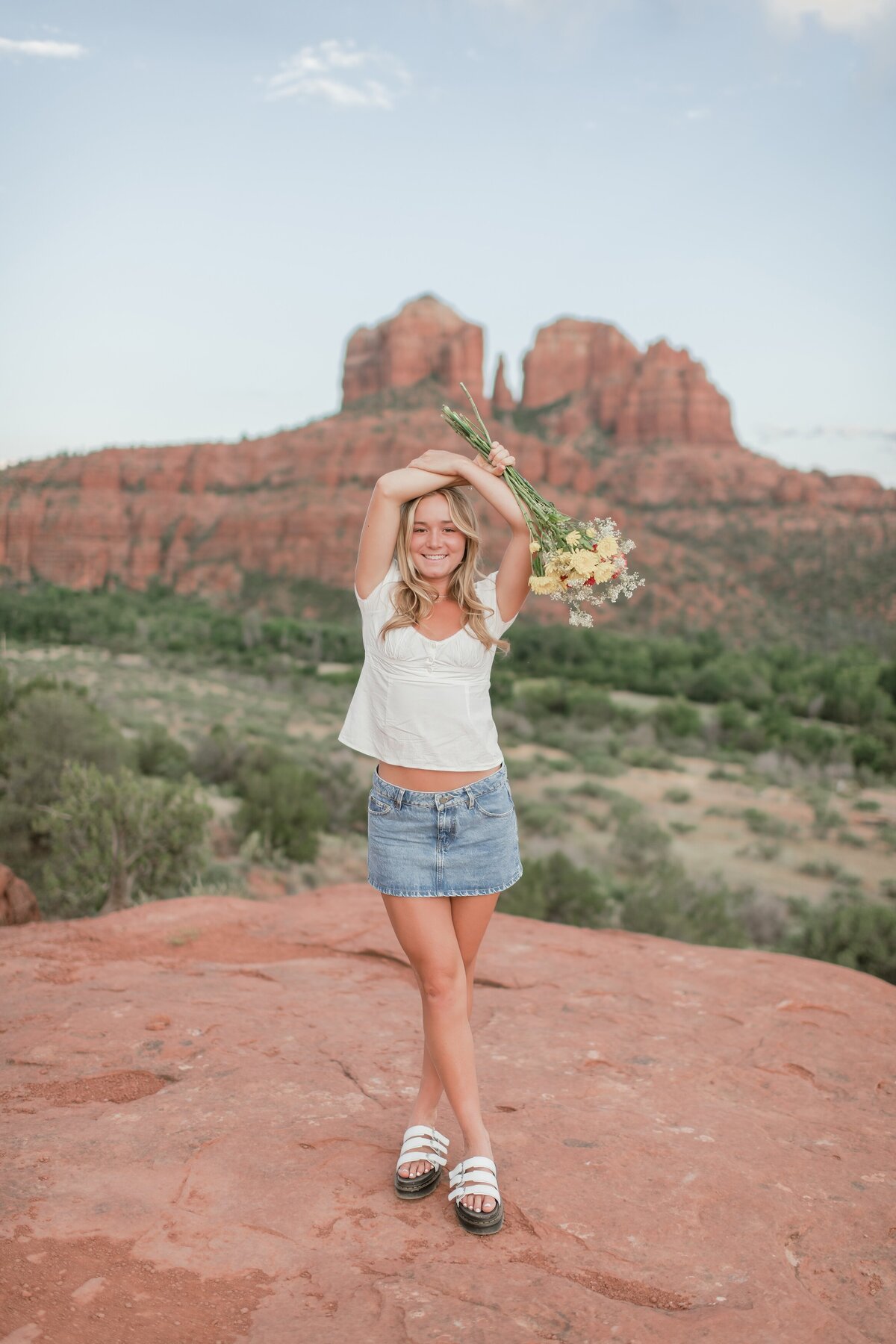senior girl standing with flowers over her head in Sedona with cathedral rock behind her