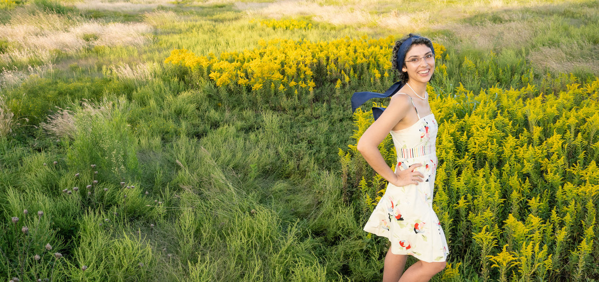 Lady in a short white floral dress stands in a field of yellow flowers