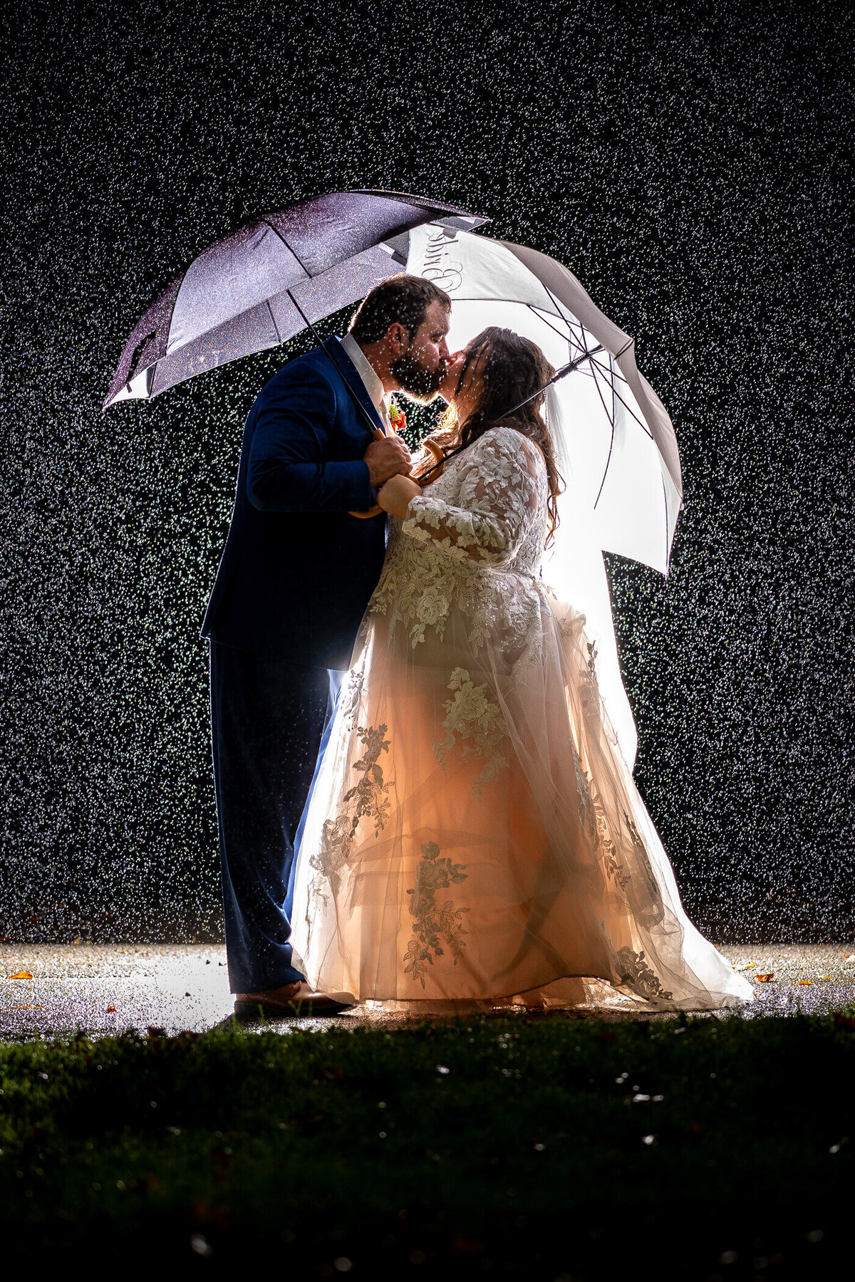 Dramatic Pittsburgh wedding photography of a couple kissing in the rain while holding umbrellas and being illuminated by flash, captured at Brady's Run Lodge in Beaver County PA
