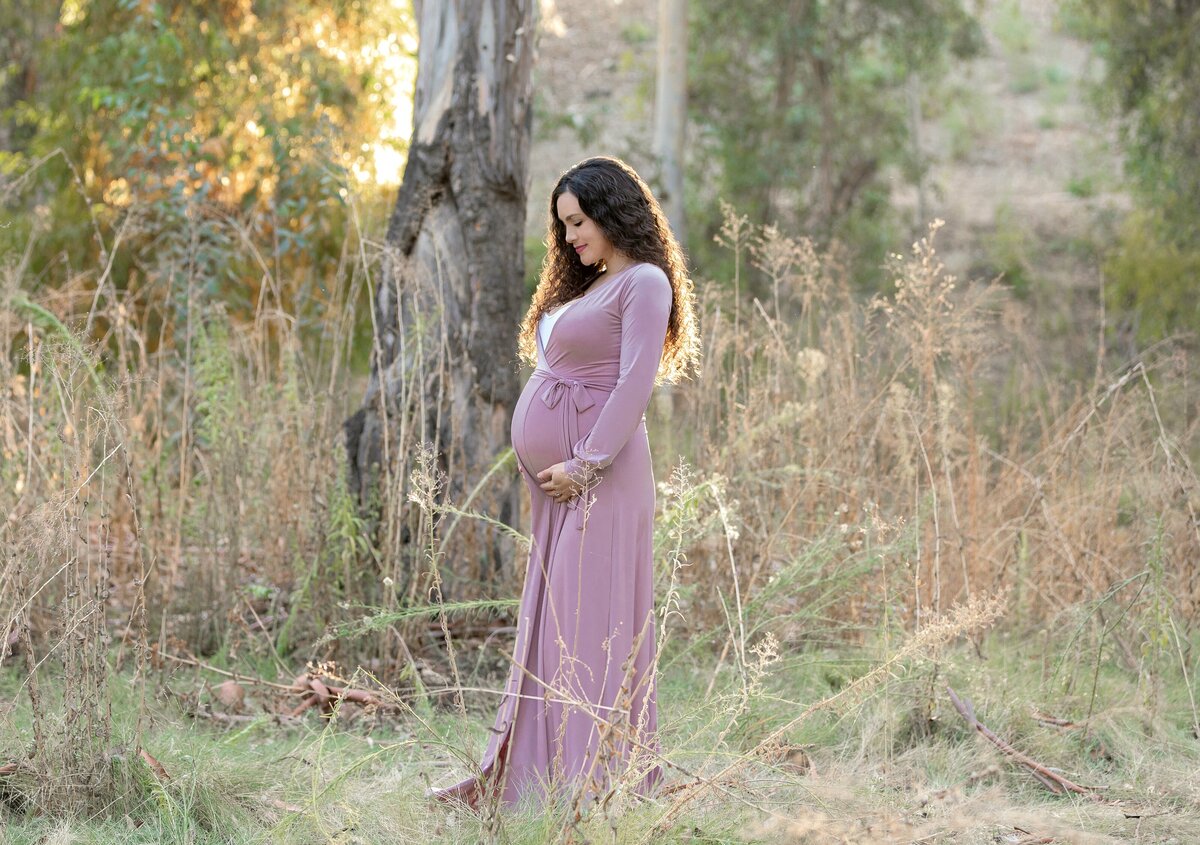 PREGNANT WOMAN IN PINK GOWN POSING IN TALL GRASS
