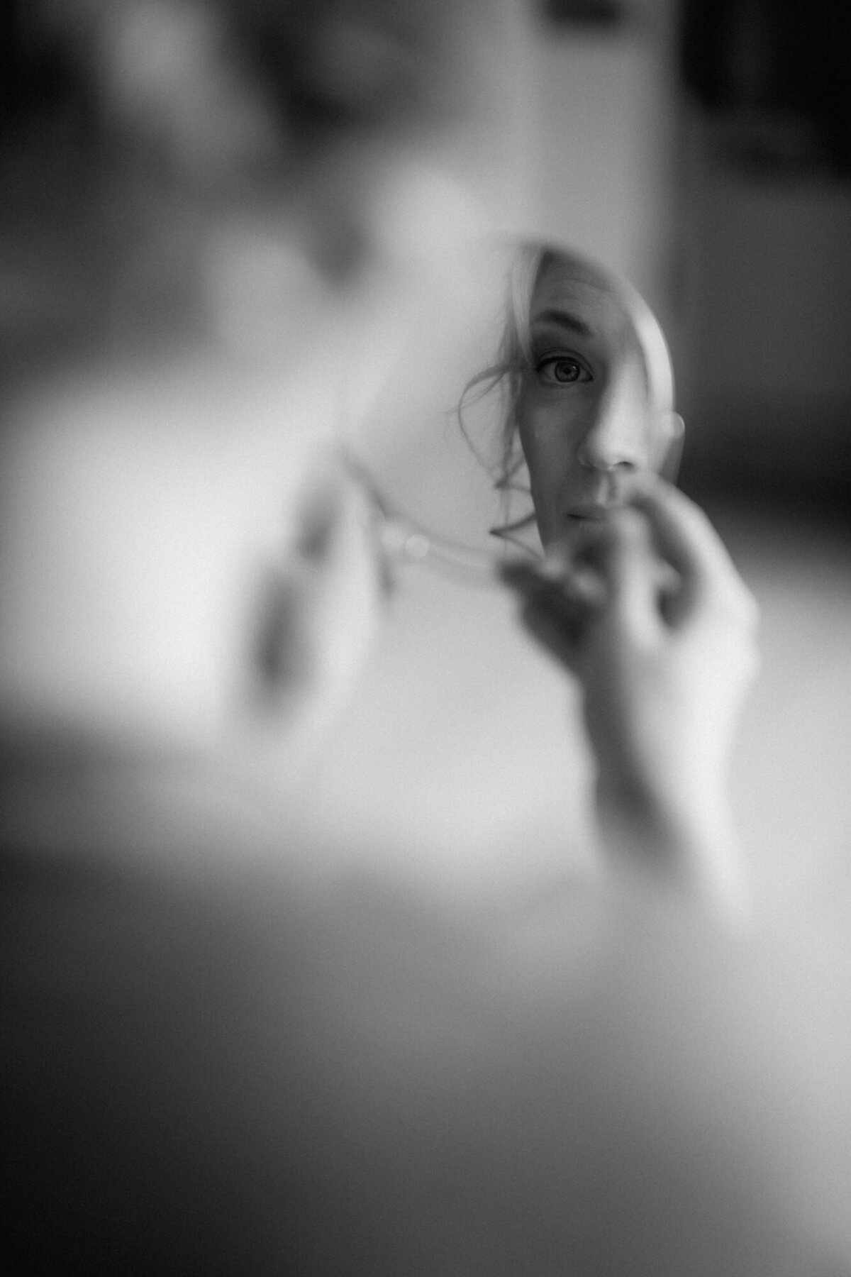 Die Braut betrachtet sich in einem kleinen runden Spiegel. Nur ihre Spiegelung ist deutlich sichtbar.