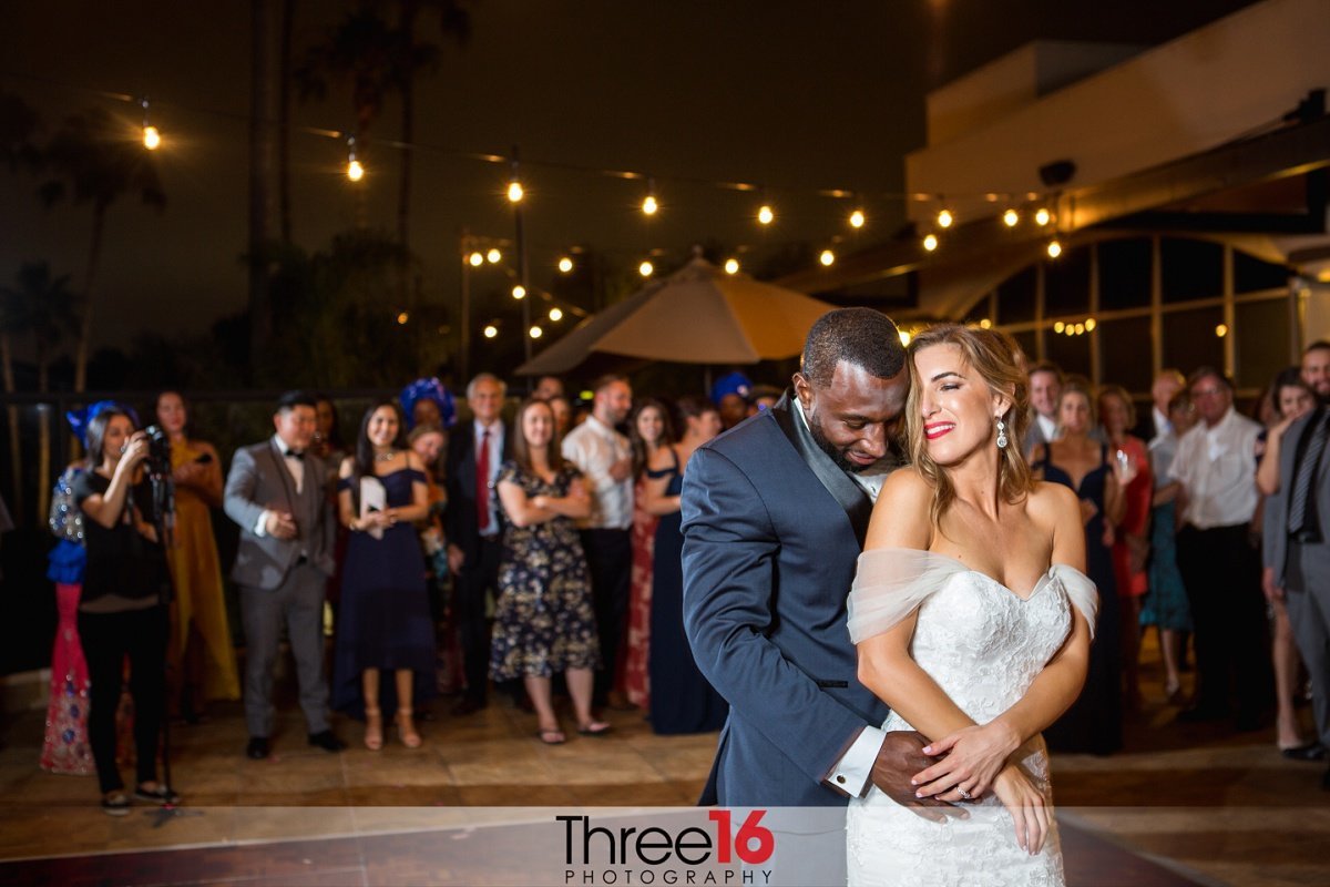 Groom embraces his Bride during first dance as guests look on