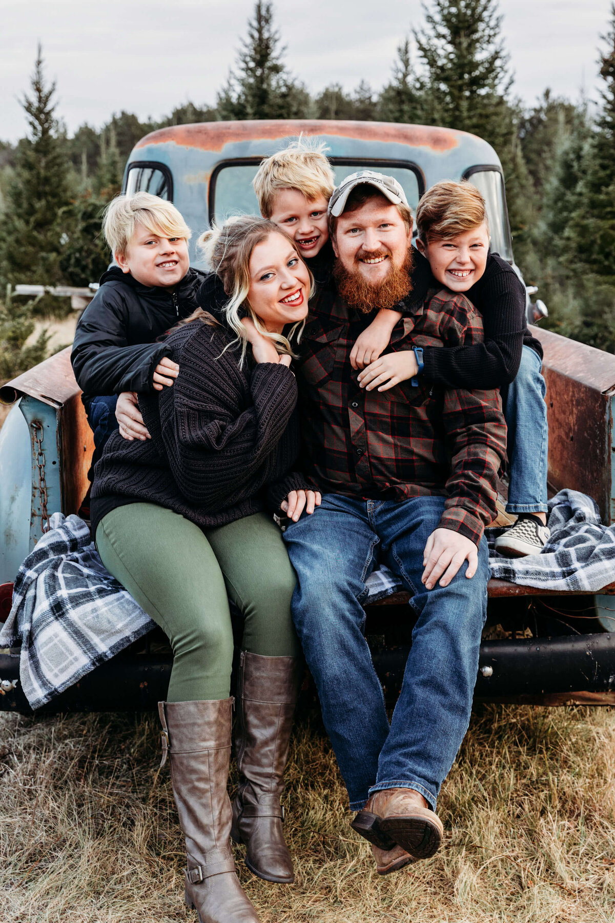 Adorable 3 boys hugging their parents from behind while sitting in a vintage truck at a tree farm during family session.