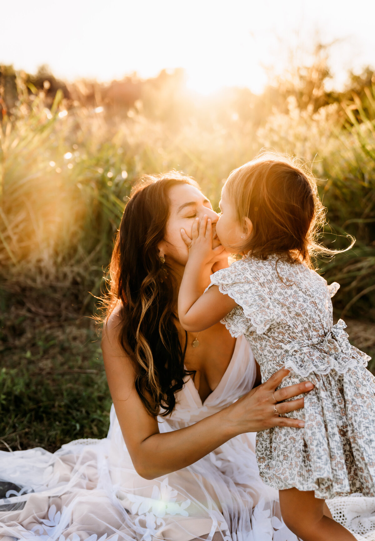 Family Photographer, mom kisses her baby girl on a blanket in the grass
