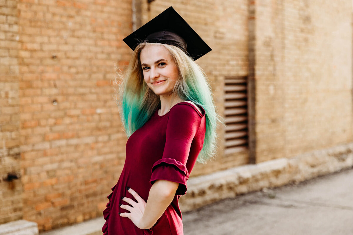 beautiful high school grad posing with  hand on her hip with grad cap on