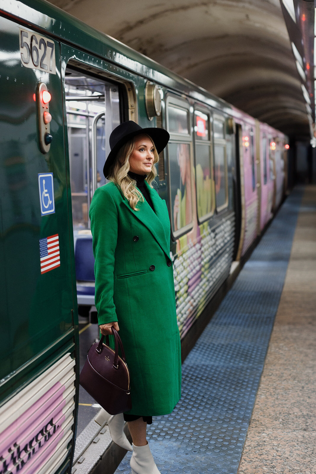 blonde woman in long green coat is stepping off the Chicago L train with a large purse in her hand.