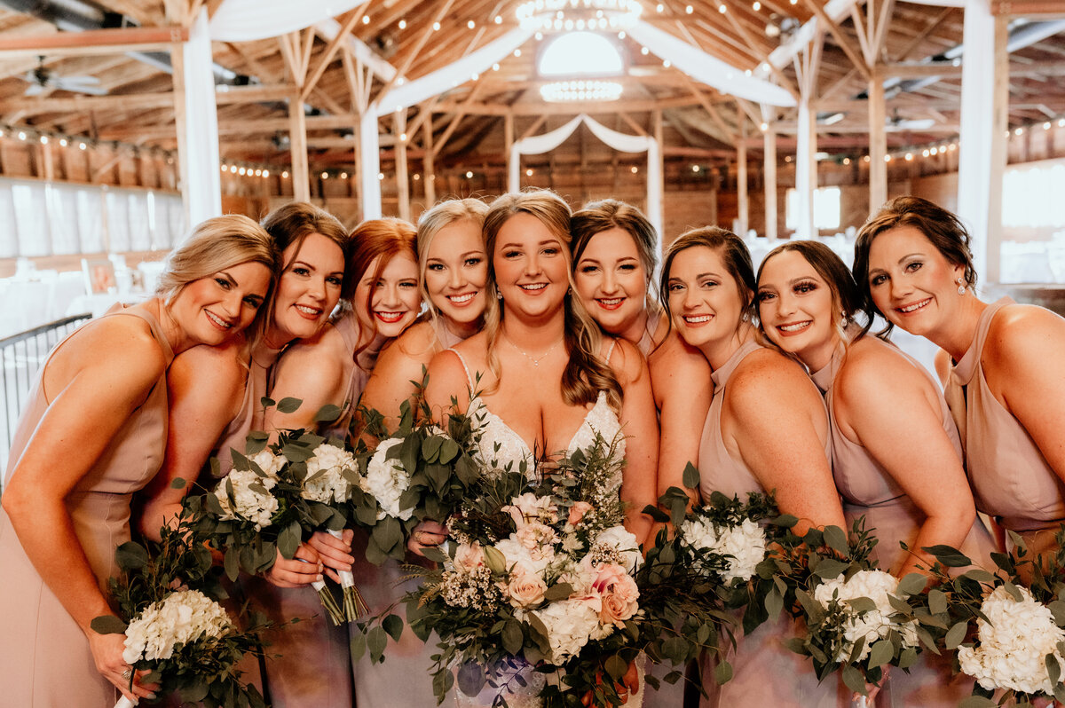 bride standing in the middle of her bridesmaids as they all hold their wedding bouquets while leaning into each other and smiling
