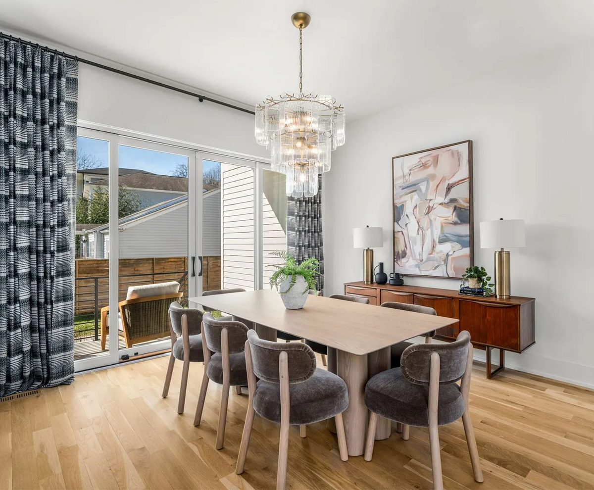 Elegant dining room with velvet chairs, light wood table, statement glass chandelier, mid-century sideboard, and abstract wall art.