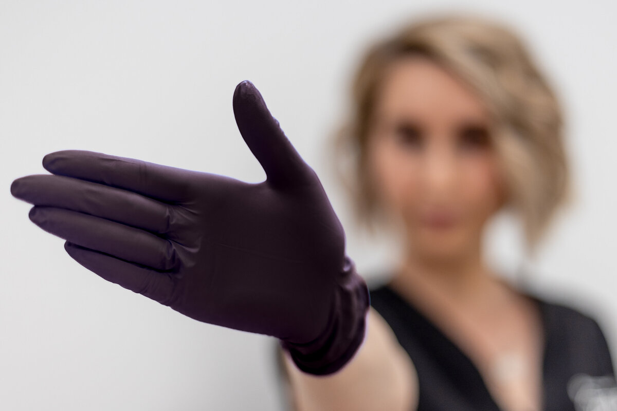 Esthetician with a black glove holding it close to camera