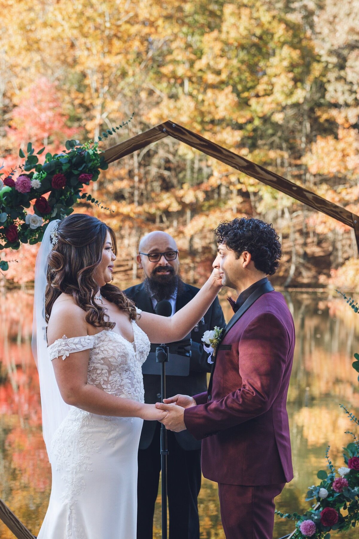 Bride and groom exchanging vows under a wooden hexagon arch.