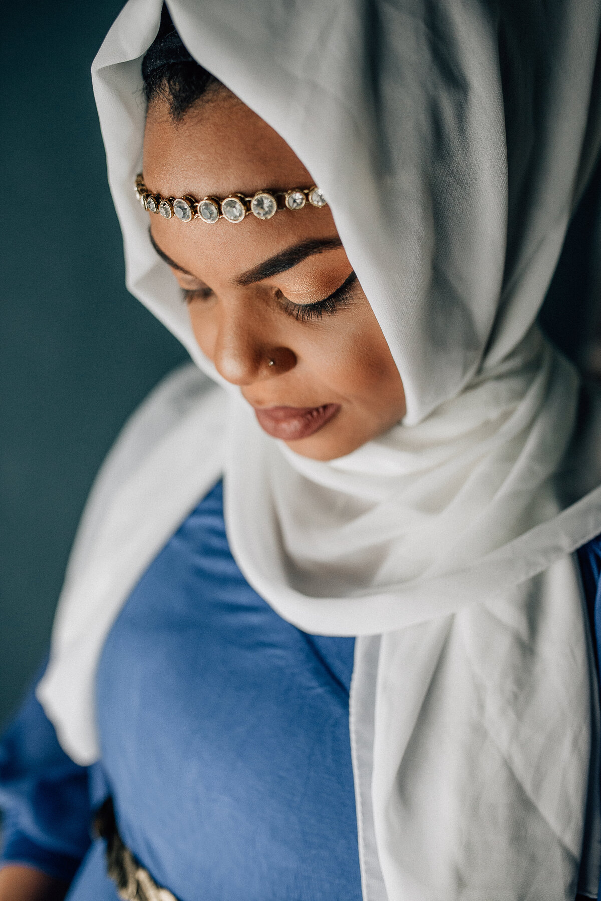Maternity shot of a mom wearing white scarf and blue dress looking down.