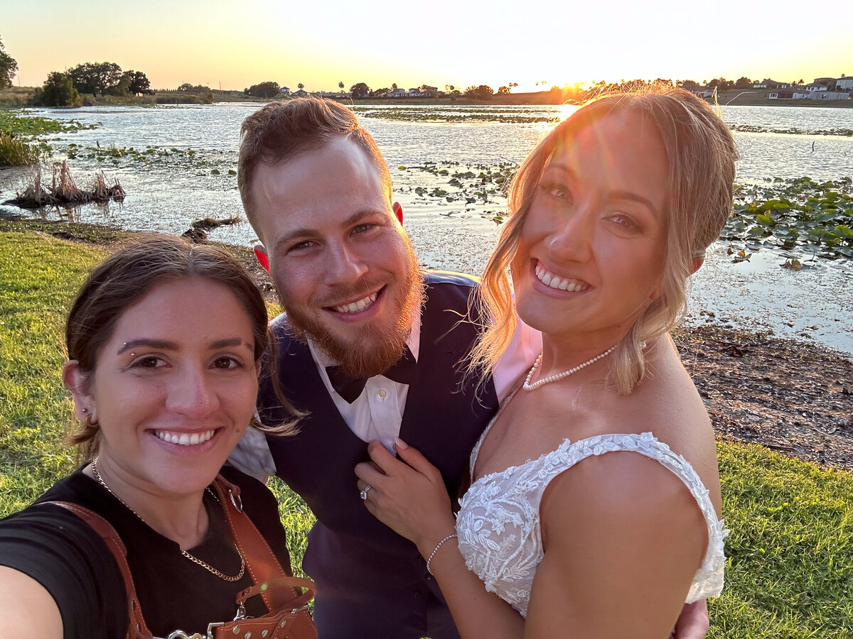 Five Star Wedding photographer smiling with a bride and groom at sunset by the lake at Adams Estate in Lake Wales, Florida.