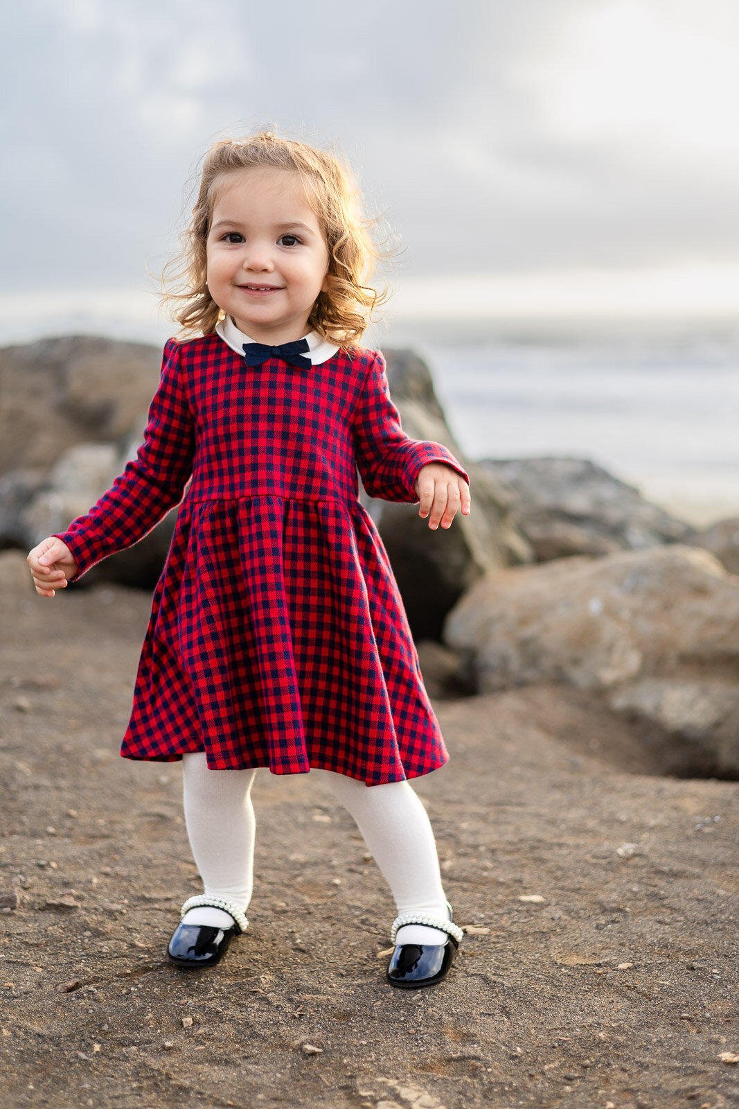 Toddler girl in red plaid dress posing near the beach for Bay Area school photography lifestyle session – Ellobelle Photography
