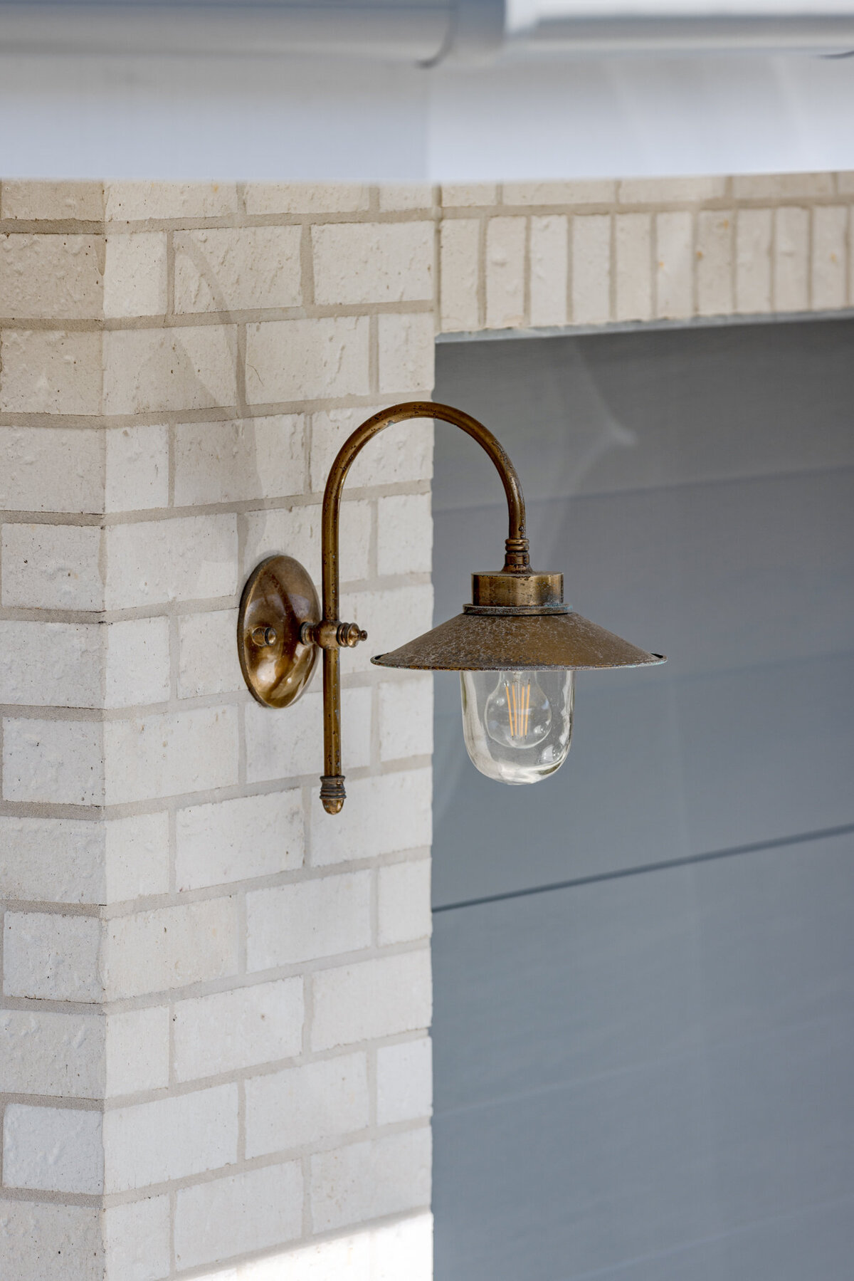 Bronze outdoor wall sconce with a clear glass shade graces the light brick wall, evoking the sophisticated touch of a Newcastle Interior Designer.