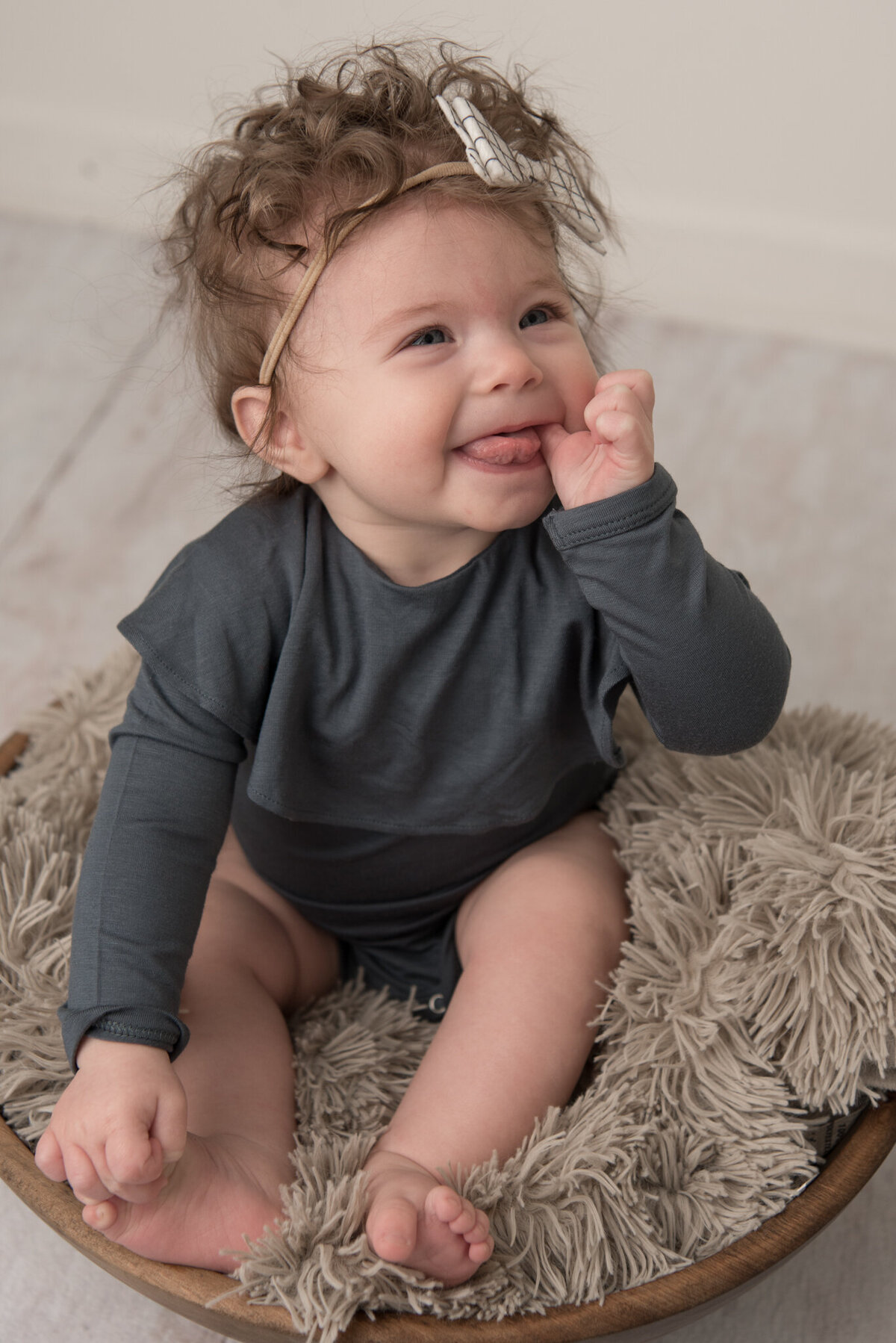 Infant girl sitting in bowl, holding toes and smiling off-camera