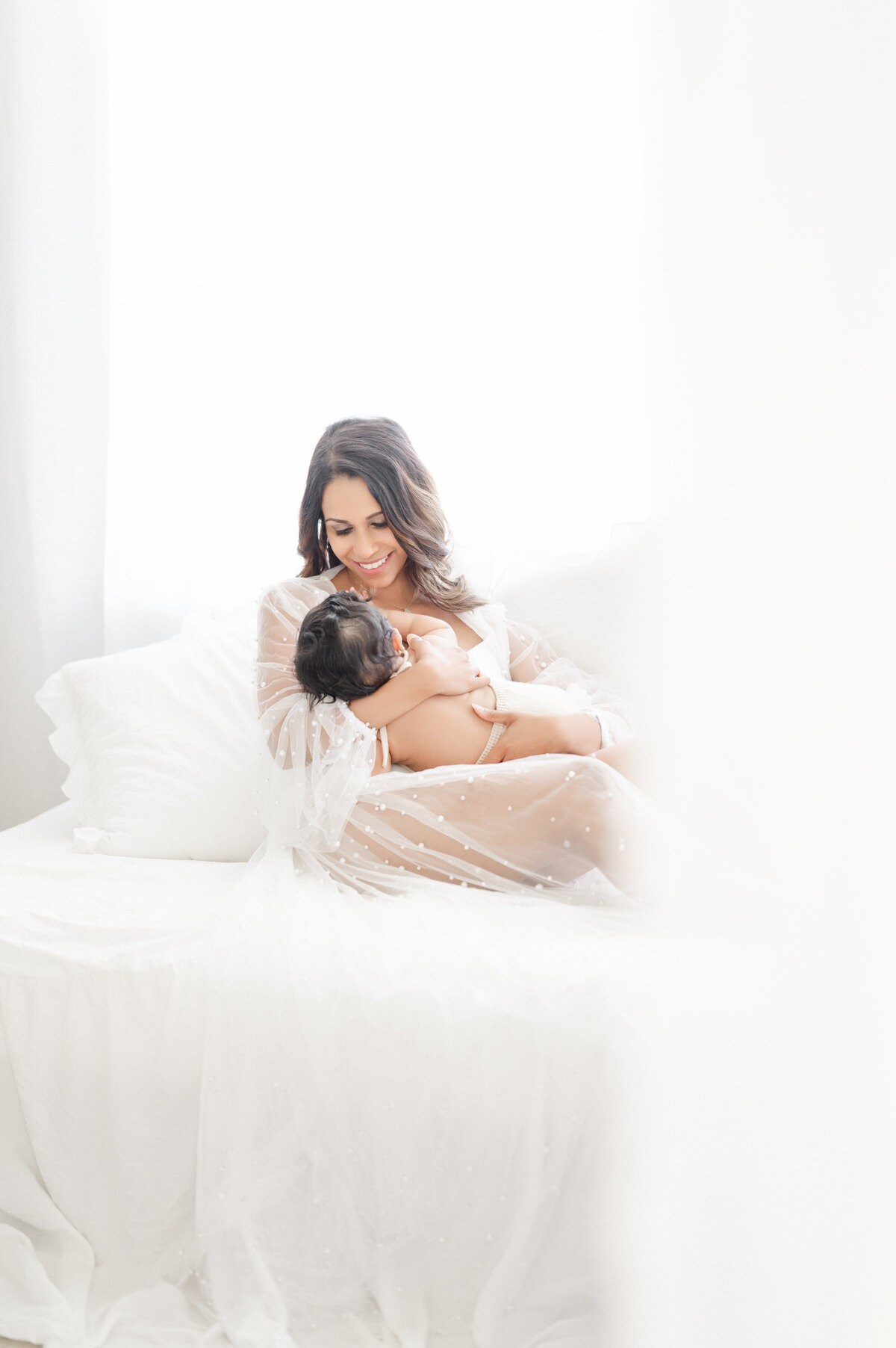 Luxury motherhood moment in Tampa studio: mother gently nursing baby in soft, editorial light
