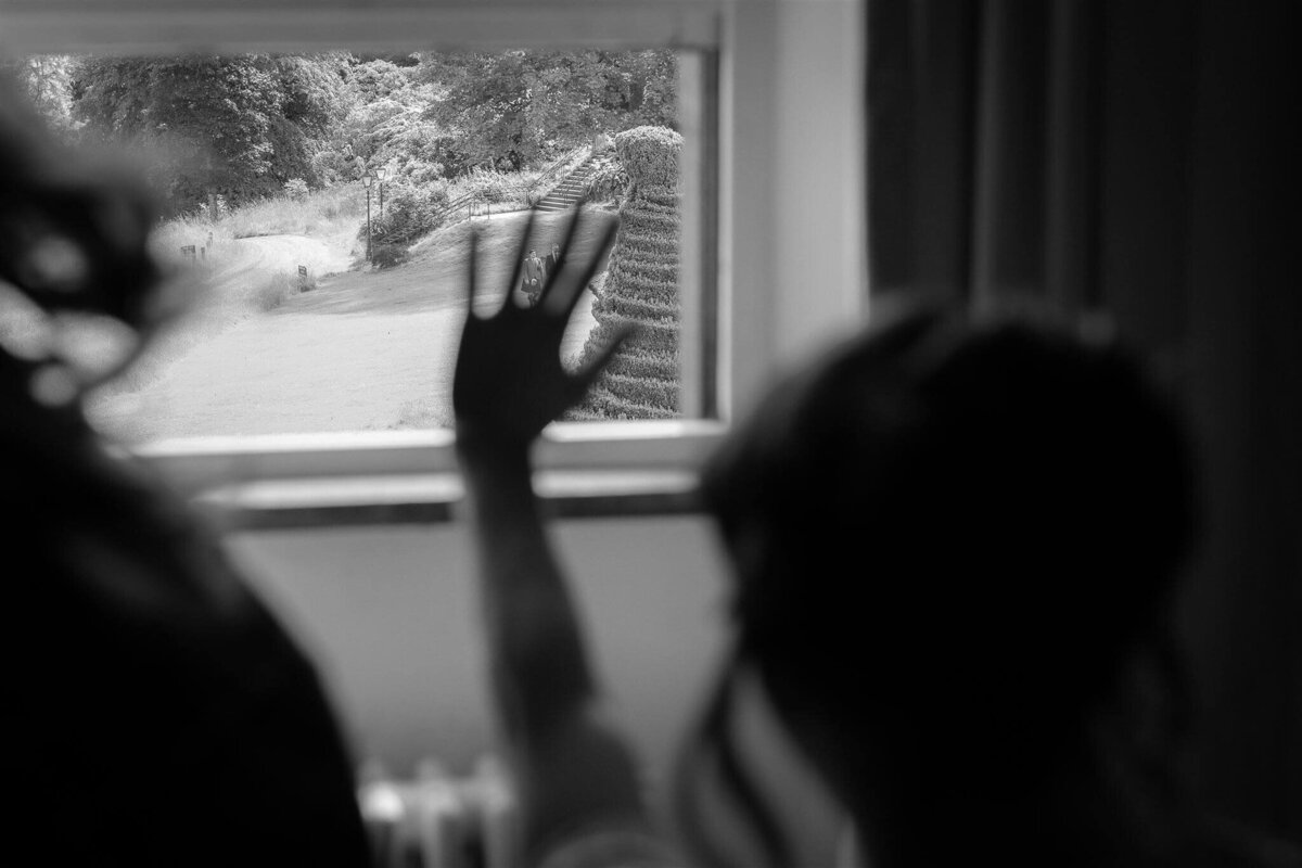 A bride waves through her window as her groom walks to the wedding ceremony.