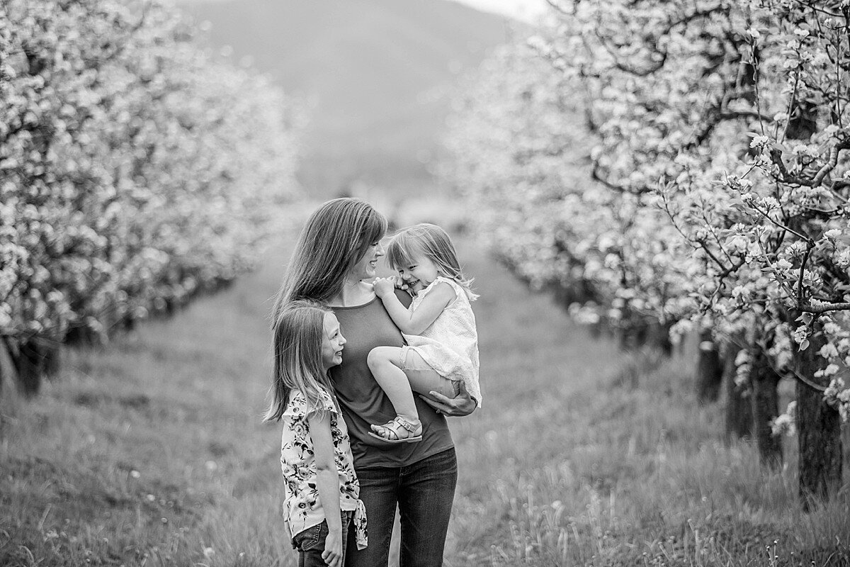 Mother holding two young daughters in orchard