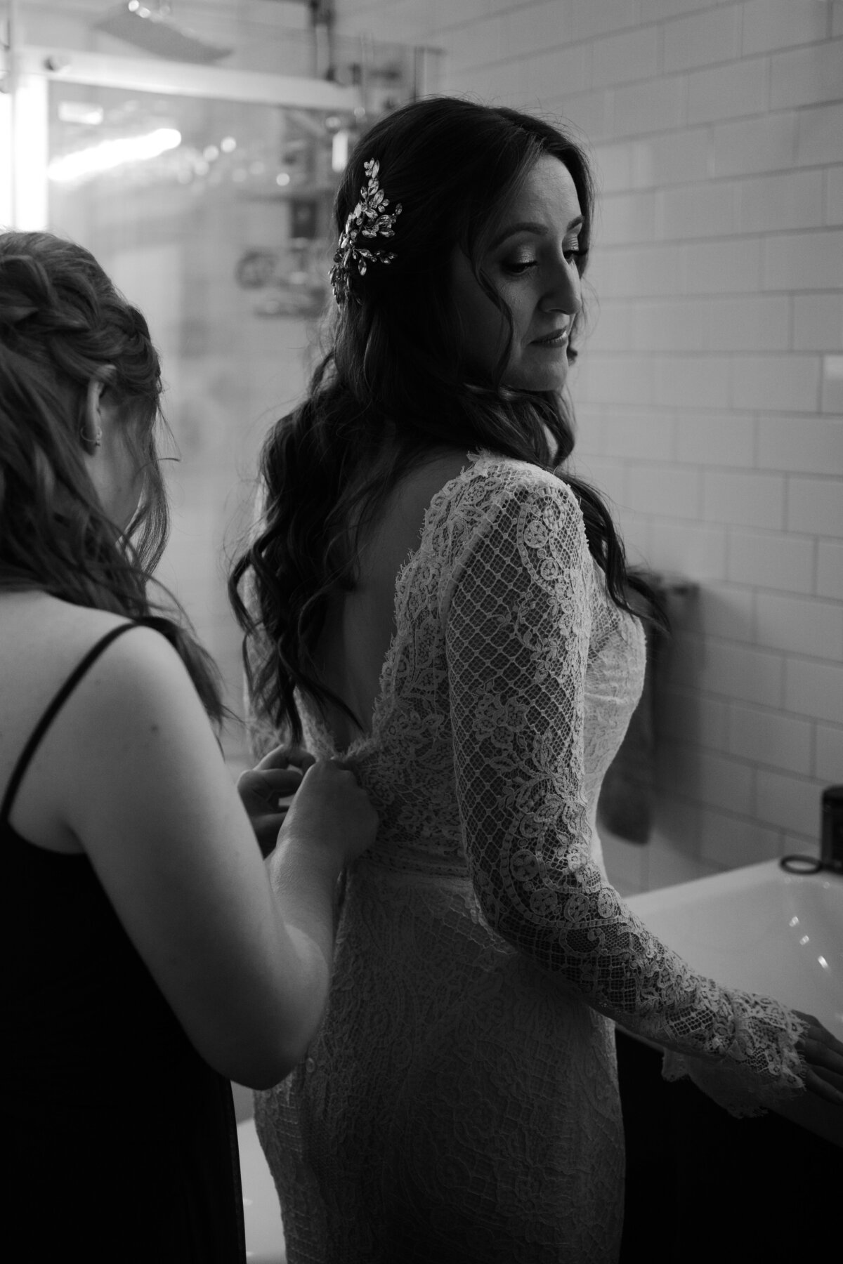 black and white image woman zipping bride's dress