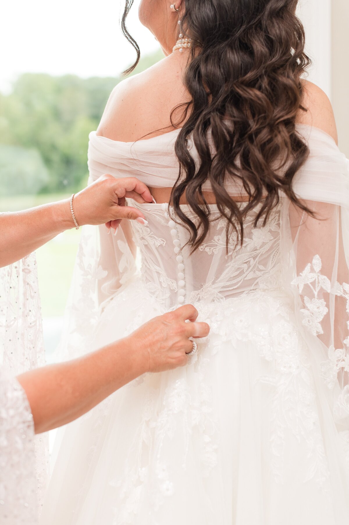 mom buttoning up daughter wedding gown