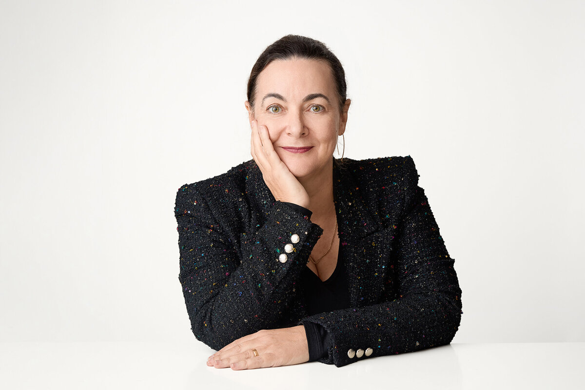 Seated woman at white desk against white background. Staring with determination at camera.
