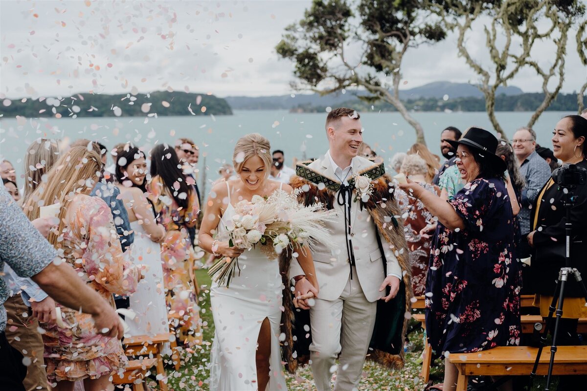A newly married modern bride and groom walking back up the aisle as their guests toss confetti and photographed by Waikato photographer Haley Adele Photography at Baylys Farm in Northland