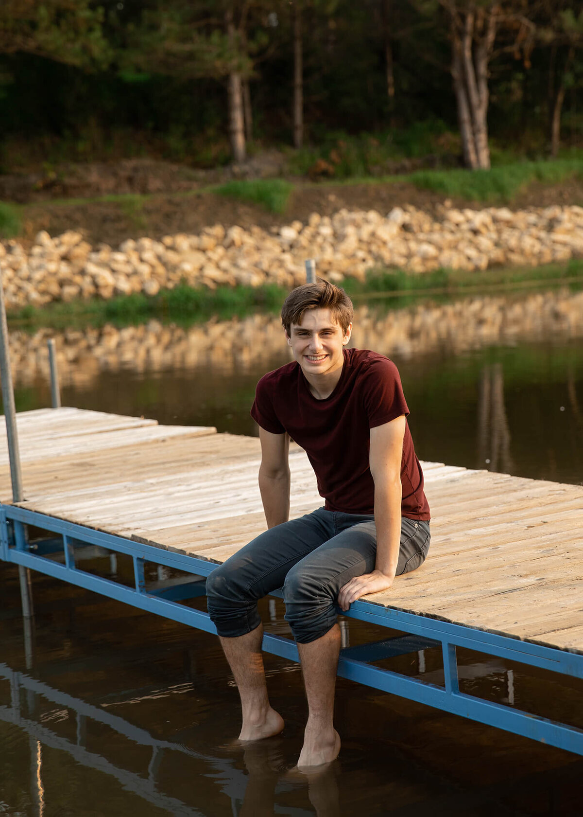 Senior boy sitting on a pier with this legs hanging into the water.