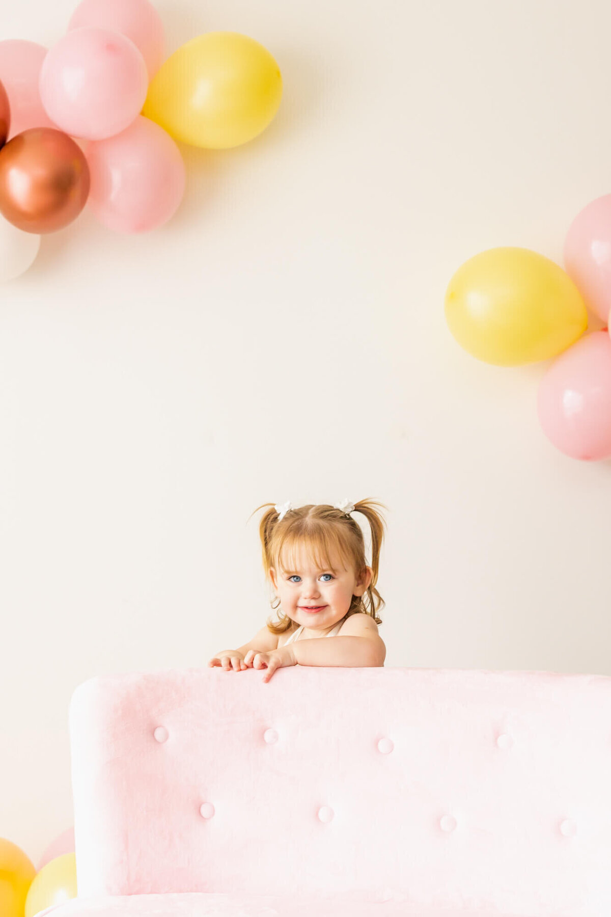 Toddler girl dresses in bell bottoms and a lace romper standing behind a pink couch