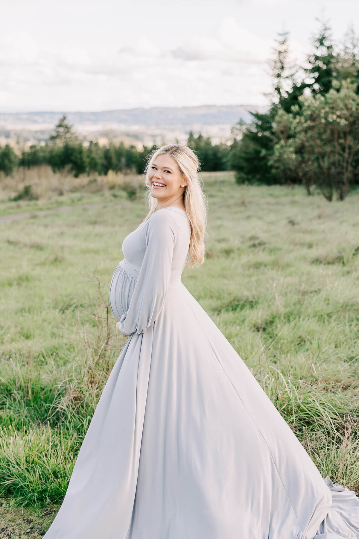 Outdoor portrait of a beautiful blonde woman holding her belly wearing a silver long sleeve dress in beaverton oregon.