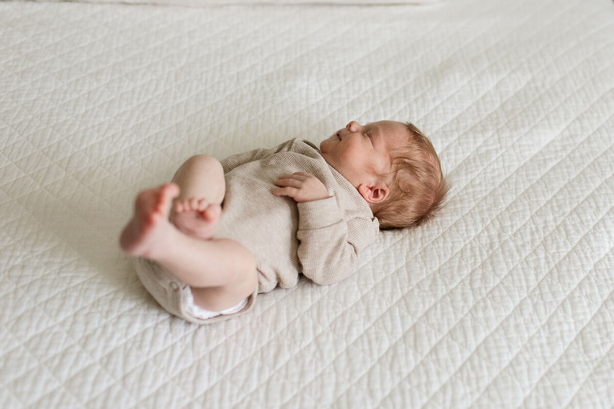 Newborn baby resting peacefully on soft bedding - Sara James creates gentle newborn portraiture and delicate infant photography during serene lifestyle sessions in San Antonio Texas family bedrooms