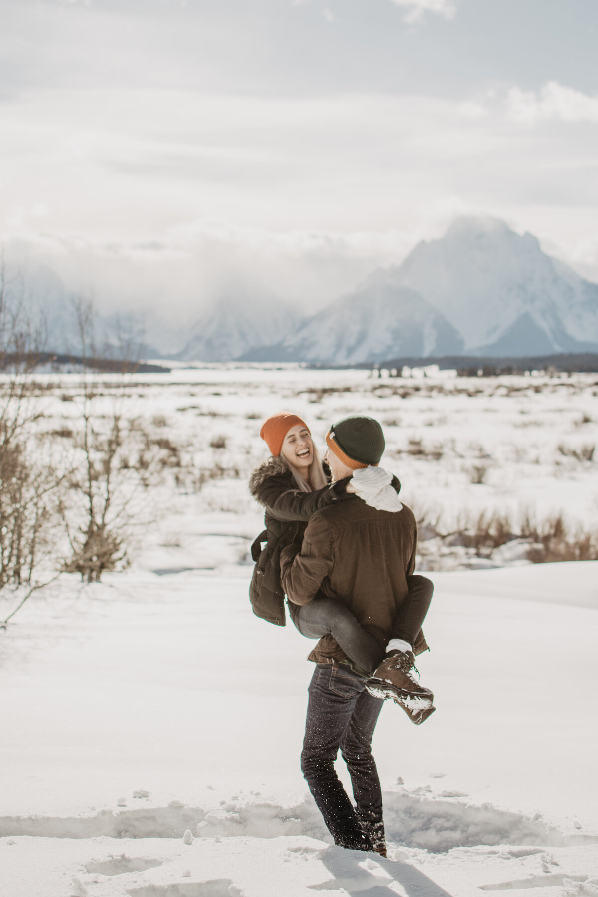 winter engagement photos in jackson with man holding his fiance in the snow  for their winter engagement session with jackson hole photographers