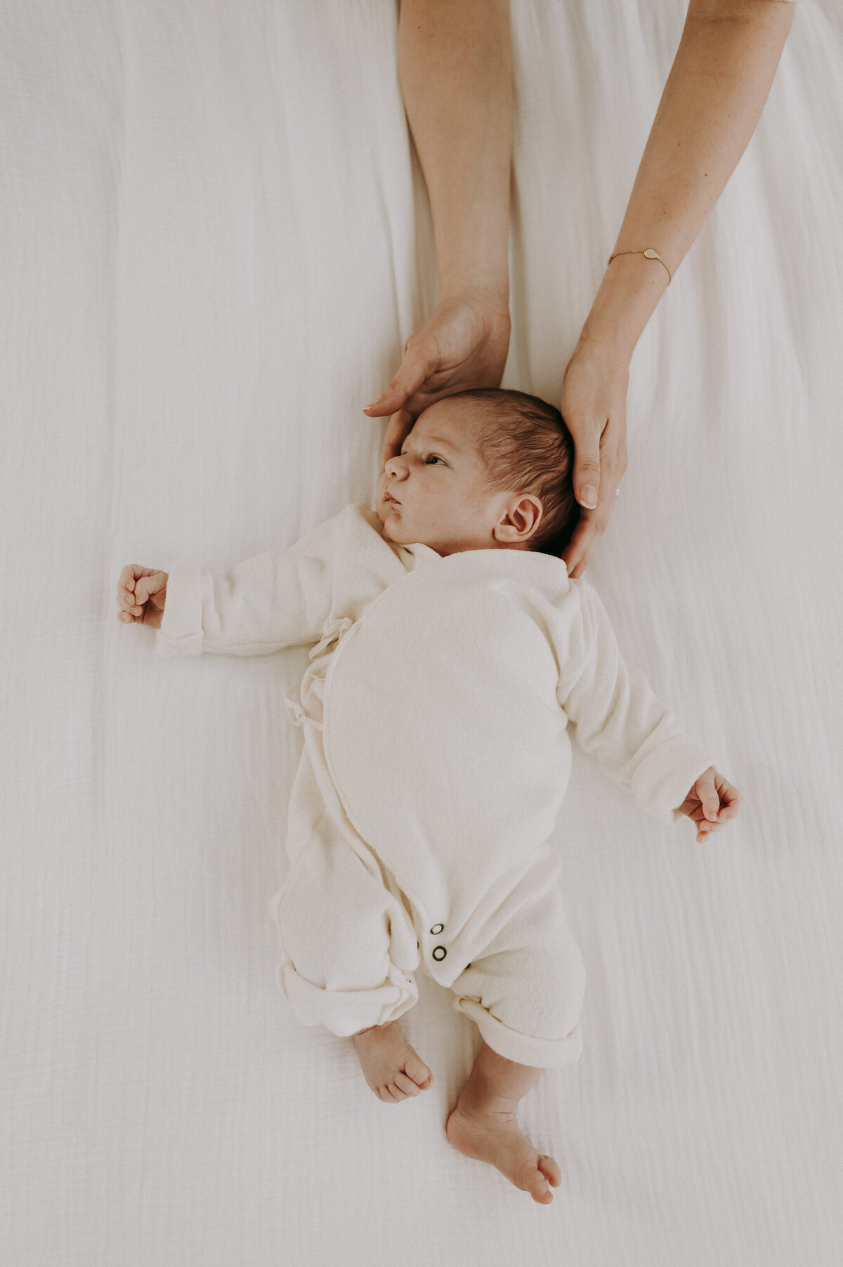 Baby ligt op het bed en ouders houden hem vast met handen.