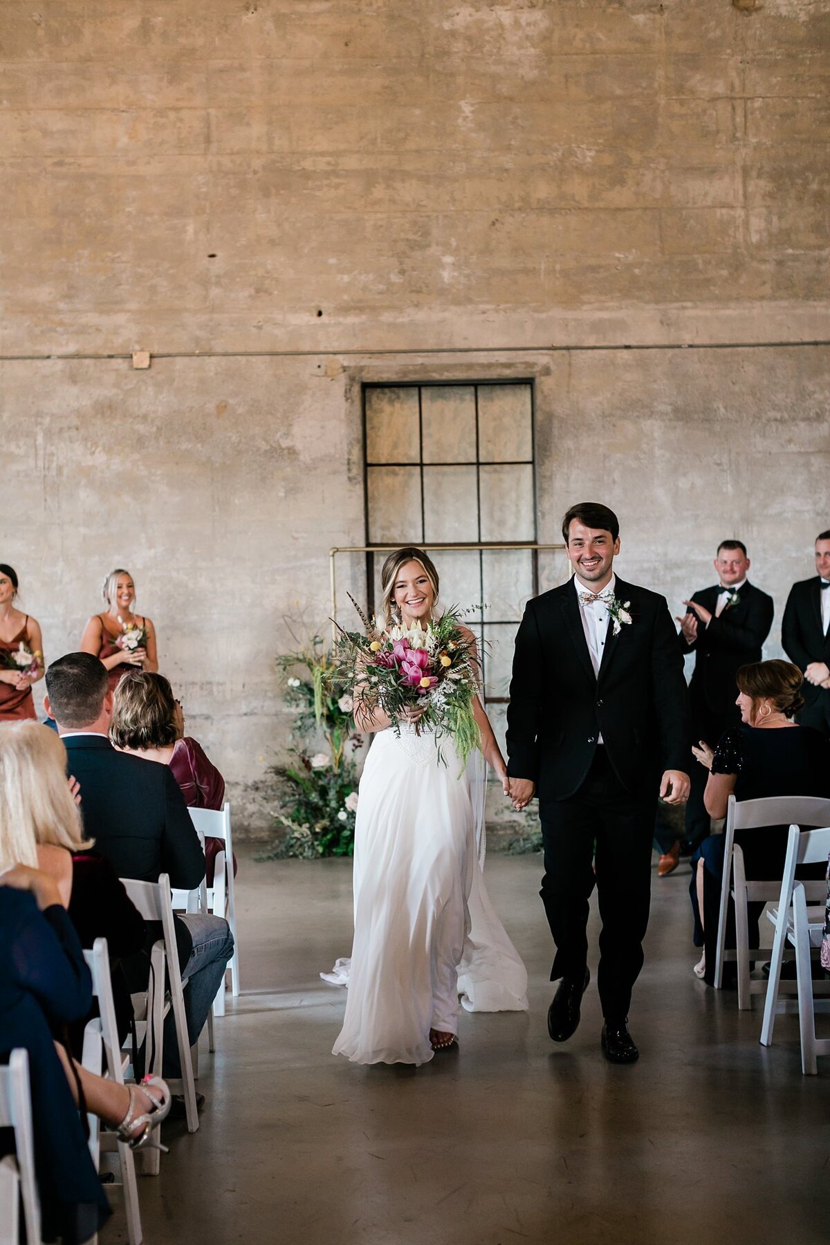 Bride and groom walking down the aisle smiling after being pronounced husband and wife with their guests cheering at Olde Dobbin Station