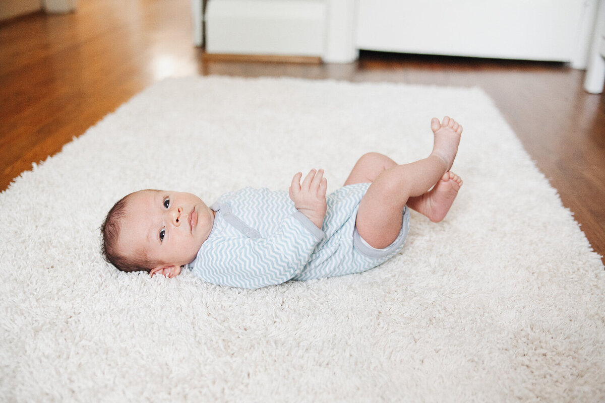 Newborn boy laying on cream rug in nursery